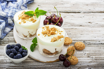 Healthy summer dessert of berry yogurt almond cookies portioned in glass cups on a light wooden background with ripe blueberries and juicy cherries. Selective focus. the concept of fitness nutrition