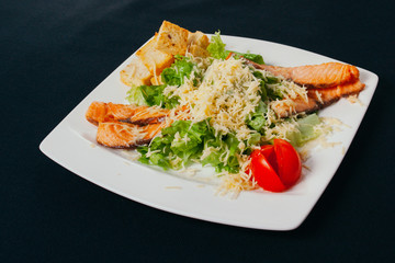 Grilled salmon with spinach and seasonal vegetables salad on white plate, black background