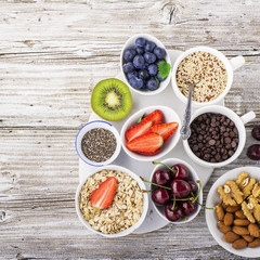 Healthy fitness food from fresh fruits, berries, greens, super food: kinoa, chia seeds, flax seed, strawberry, blueberry, kiwi, cherry, almonds, walnuts, mint, oatmeal natural flakes on a light marble
