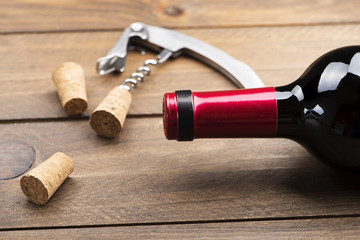 Corkscrew next to several corks and a bottle of wine on wooden table. Horizontal studio shot.