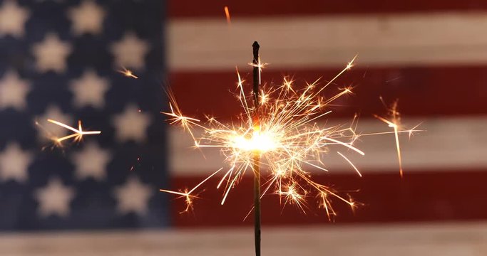 Burning sparkler with rustic wooden United States Flag in background for Independence Day celebration. 