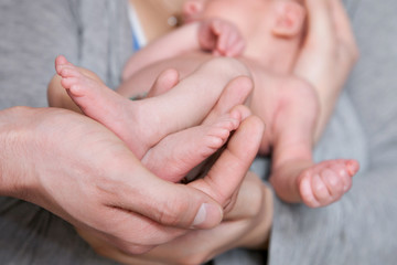 Obraz na płótnie Canvas The hands of the father hold the legs of the newborn son