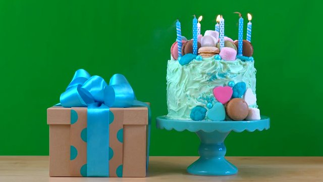 4k Green screen with blue showstopper cake decorated with marshmallows, candy and macaron cookies, and beautifully wrapped gift, blowing out candles.