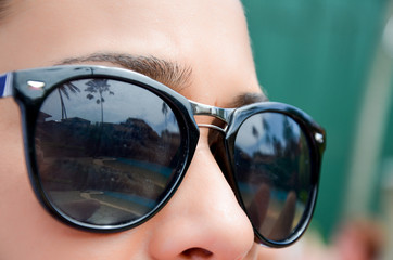 Close-up of glasses on girl with reflection of palm trees