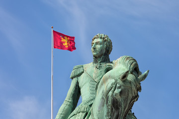 Obraz premium Statue of former Swedish King Karl XIV Johan with the Royal Standard of Norway flag in background at the royal palace of Oslo symbolising that the present king is 
