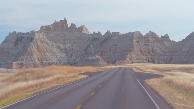 FPV: Driving along the empty road towards the picturesque Badlands landscape with rocky sandstone formations. Traveling across the Badlands desert in South Dakota. Road trip across United States.