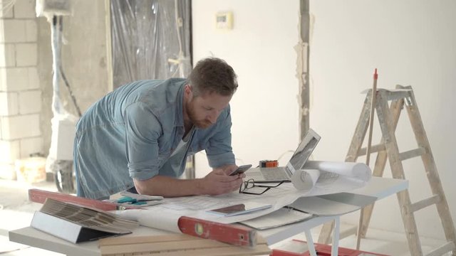 Man standing in his new flat and texting messages on smartphone, steadycam shot
