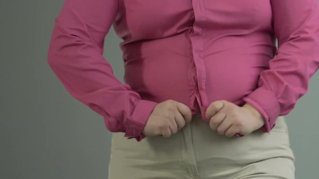 Oversized girl hopelessly trying to button small shirt, weight control problem