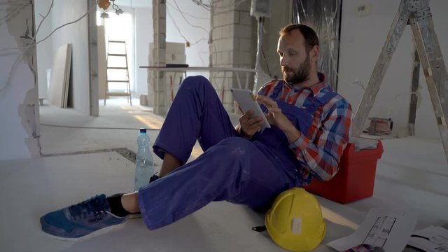Worker sitting on the floor in his new flat and using tablet, steadycam shot
