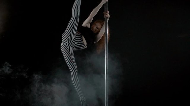 The girl is dancing Pole Dance on dark backgroun, in studio with smoke