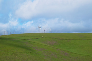 Fototapeta na wymiar Wind turbines on a hillside, against the backdrop of cloud-filled blue sky in the Livermore, California wind farm