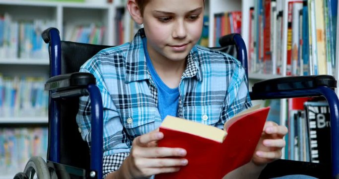 Disabled schoolboy on wheelchair reading book in library