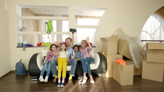 Family taking selfie, waving hands. Happy people near cardboard boxes. How to start vlogging.
