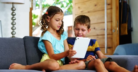 Siblings using digital tablet in living room - Powered by Adobe