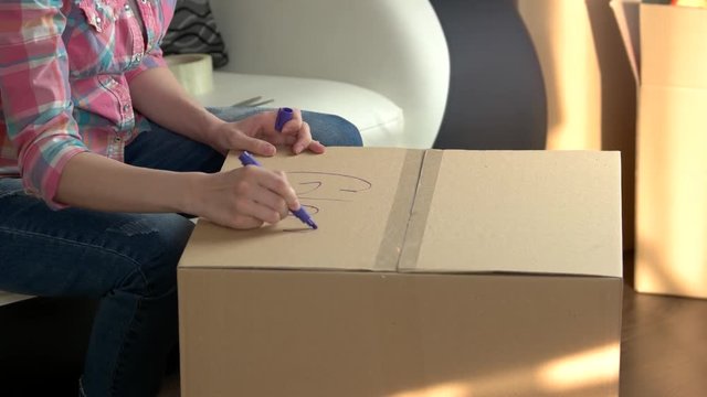 Woman quickly packing box. Hand writing with a marker.