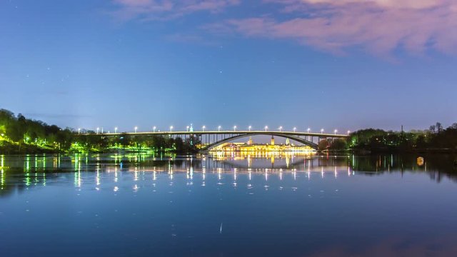 Tranquil bay and arch bridge at night 4K Time Lapse. Stockholm cityscape in background, beautiful reflections in the water