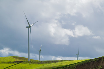 Fototapeta premium Wind turbines on a hillside, against the backdrop of cloud-filled blue sky in the Livermore, California wind farm
