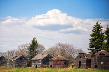 Fototapeta na wymiar A row of old weathered square wooden sheds and crumbling antique grain storage bins under cloudy sky in rural countryside landscape