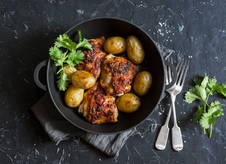 One pot baked harissa chicken and new potatoes on a dark background, top view