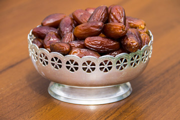 Dates fruit on a silver bowl on wooden table. The Muslim feast of the holy month of Ramadan Kareem