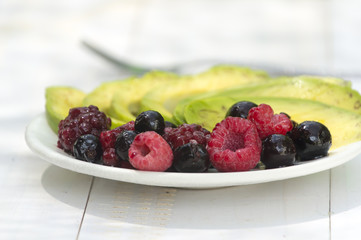 Healthy breakfast ingredients avocado slices with mix berries and honey.