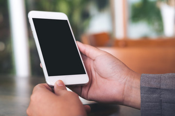 Mockup image of hands holding white mobile phone with blank white screen with on wooden table in cafe