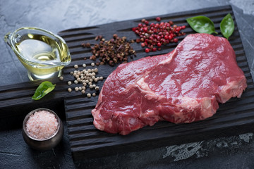 Close-up of raw fresh ribeye beefsteak with different types of pepper, pink salt and olive oil, selective focus