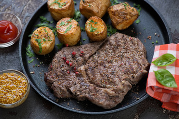 Close-up of grilled ribeye beef steak with baked potato, selective focus, studio shot