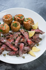 White plate with grilled tagliata beef steak and whole baked potatoes, close-up, vertical shot