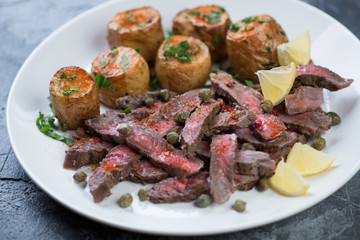 Close-up of beef steak tagliata served with baked potato on a white glass plate, selective focus