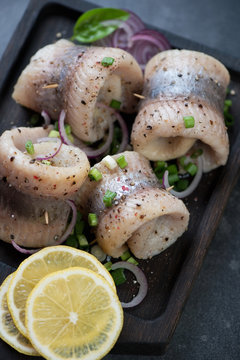 Closeup of herring fillet rolls with spices, red and green onion, and lemon, vertical shot