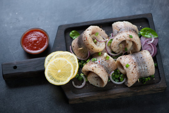 Black wooden serving tray with herring fillet rolls, onion and lemon, studio shot