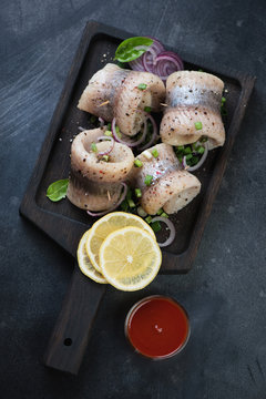 Herring rolls served with onion, spices and lemon in a wooden tray. Above view on a dark metal background