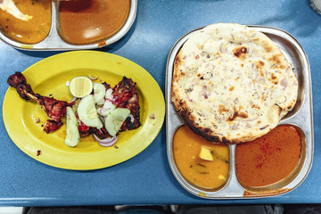 Roasted chicken with sliced cucumber, shallot and lime on yellow plate with garlic naan and curry dipping sauce in Kuala Lumnpur, Malaysia.