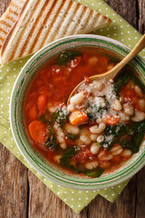 White bean soup with tomatoes, spinach, carrots and parmesan close-up on the table. Vertical top view
