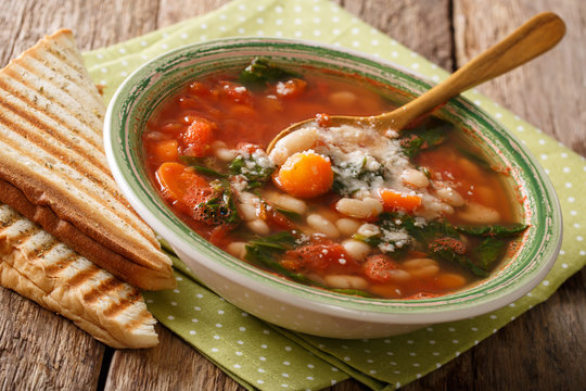 Italian soup with white beans, tomatoes, spinach, carrots and parmesan close-up. horizontal 