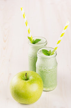 Freshly blended green apple fruit smoothie in glass jars with straw, mint leafs, apples. White wooden board background, copy space.