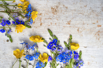 Frame from two small bouquets of wild flowers, buttercup and forget me not on the old painted white wooden background, top view, with copy space for your text