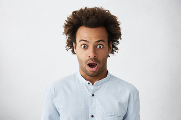 Studio portrait of bug-eyed dark-skinned man with bushy dark hair and bristle looking with surprise...