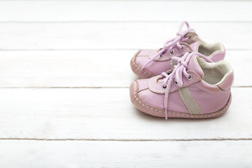 Pink little shoes for a girl on a white wooden background