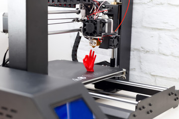 A hand made of red plastic, printed on a printer, stands on the printer