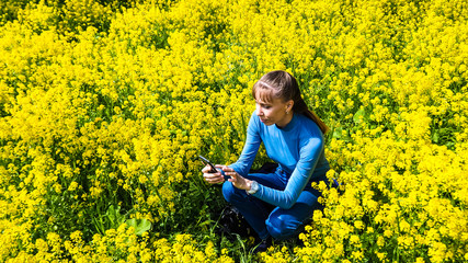 Fototapeta premium Woman holding mobile phone on the lawn of yellow flowers. 