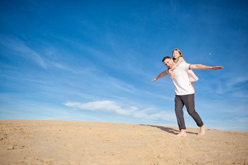 Dad and little girl daughter playing on the beach, fly, run, laugh at the blue sky background