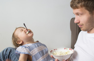 Dad feeds the baby porridge. The child does not want to eat porridge. Young father