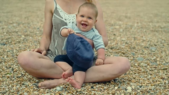 Smiling baby on the beach doesn't want to wear his hat