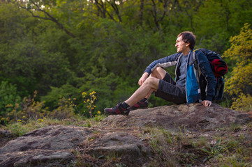 Naklejka na ściany i meble Man backpacker looking forward hiking in summer forest and stopped to have rest. Travel, hiking, backpacking, tourism and people concept