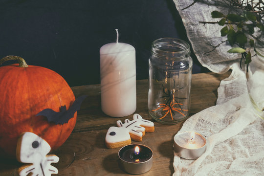 Halloween home decorations with candles, spiders, pumpkin, cookies and jar for  treat and black berries. Dark background. Shallow depth of field. Toned