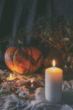 Halloween home decorations with candles, spiders, pumpkin, cookies and jar for treat and black berries. Dark background. Shallow depth of field. Toned