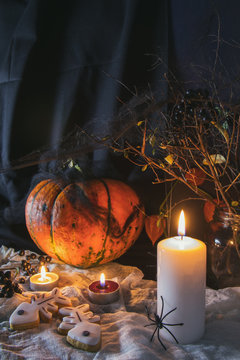 Halloween home decorations with candles, spiders, pumpkin, cookies and jar for  treat and black berries. Dark background. Shallow depth of field. Toned