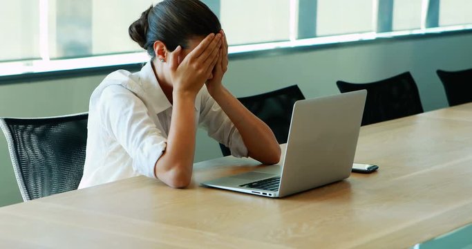 Executive crying while working on laptop in conference room